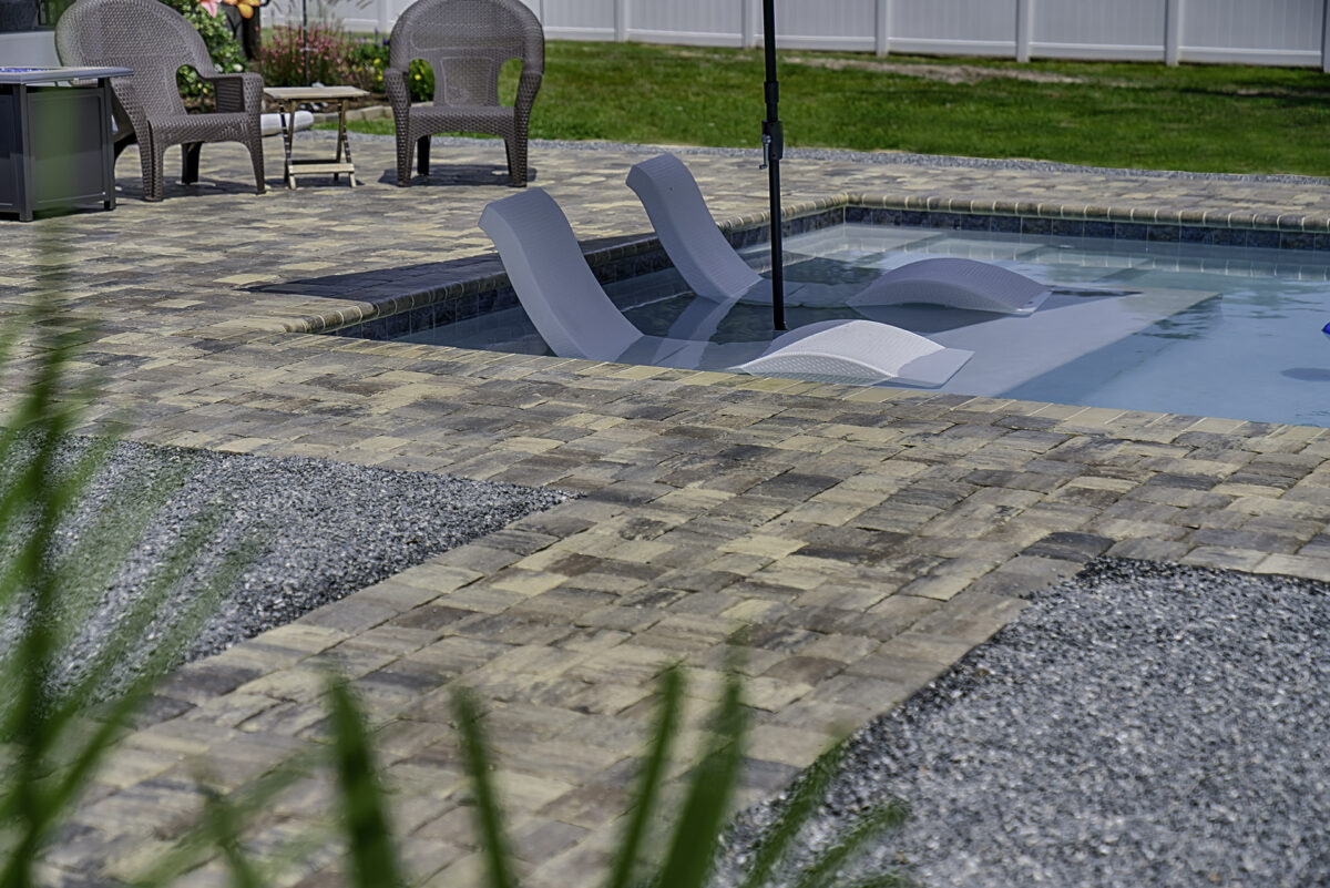 View of a brick walkway leading to a pool with two lounge chairs sitting in the water